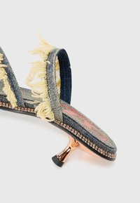 Denim glidesandal med frynser, en rosa logo på sålen og en reflekterende metallhæl med et svart gummitipp.