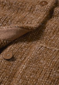 Nahaufnahme eines braunen Wollstrickstoffs mit strukturiertem Stichmuster und braunen Knöpfen auf einem gefalteten Kleidungsstück.