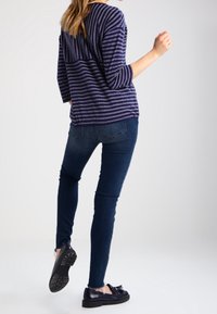 Top rayado de color navy con mangas tres cuartos, combinado con jeans ajustados de color azul oscuro y zapatos negros con suela texturizada.