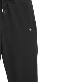 Schwarze Jogginghose aus weichem Stoff, mit elastischem Bund und Kordelzug, Seitentaschen und einem kleinen Logo am Oberschenkel.