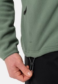 Pullover in pile verde tenue con finitura testurizzata. Presenta una tasca sul petto, un cordino regolabile all'orlo e polsini aderenti.