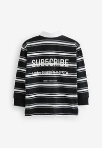 Camicia a maniche lunghe a righe bianche e nere con colletto bianco. Il testo sul retro include "SUB5CRIBE," coordinate geografiche e "TWENTY FOUR SEVEN."