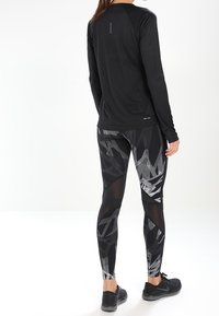 Maglietta nera a maniche lunghe e leggings a fantasia con texture in tonalità di nero e grigio. L'outfit presenta un design elegante e una vestibilità aderente.