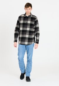 Zwart en grijs geruite overhemd met een knoopsluiting, lange mouwen en een ontspannen pasvorm, gecombineerd met lichtblauwe jeans en zwarte schoenen.