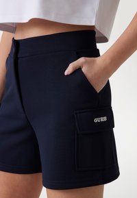 Pantaloni corti blu navy con vita aderente, dotati di una tasca laterale e etichetta ricamata. Il tessuto ha una finitura testurizzata.