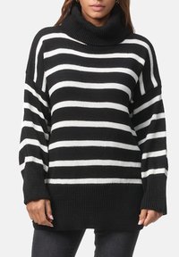 Maglione oversize a righe bianche e nere con collo alto e polsini a costine. Tessuto lavorato a maglia strutturata con maniche lunghe e vestibilità morbida.