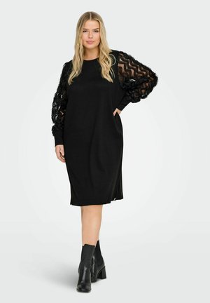 Czarna sukienka z teksturowanymi, przezroczystymi długimi rękawami. Charakteryzuje się luźnym krojem i bocznymi kieszeniami, uzupełniona botkami z grubym obcasem.