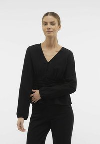 Maglietta nera a maniche lunghe con scollo a V, vita arricciata e dettagli con bottoni. Tessuto morbido con una texture liscia, abbinata a pantaloni neri a vita alta.