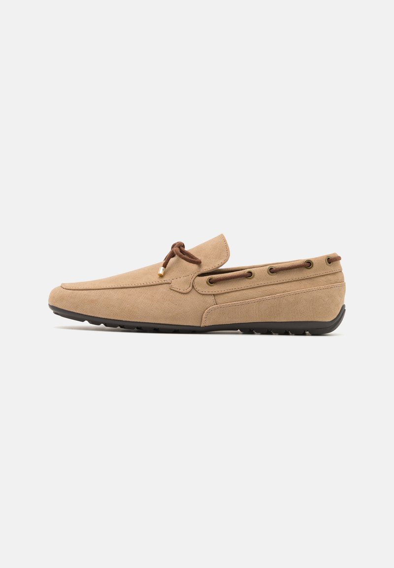 Suede loafers in light beige with a textured pattern, featuring brown laces, metal eyelets, and a flexible black rubber sole.