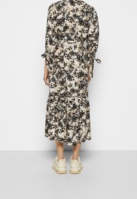 Kukkakuvioinen midi-mekko pitkillä hihoilla, vyötäröllä vyö ja kerroksellinen hameosa; kerma tausta mustilla ja ruskeilla kukkakuvioilla. Viimeistelty lenkkareilla.