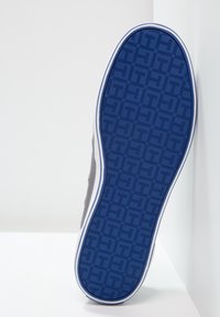 Suola di sneaker grigia con un motivo testurizzato blu e accenti bianchi lungo il bordo. Il design include un motivo geometrico per la trazione.