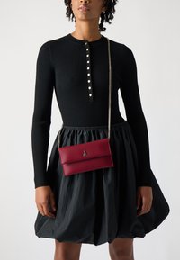 Rød skinn crossover-bag med en sølvkjede-rem, en glatt overflate og en fold-over design, med en logo-detalj på forsiden.