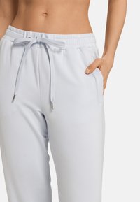 Ljusblåa sweatpants med elastiskt midjeband, dragsko och sidofickor. Materialet verkar mjukt med en slät yta.