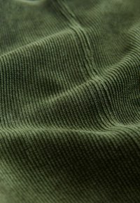 Tissu texturé vert olive foncé, présentant des côtes verticales et une surface douce et pelucheuse, créant une apparence chaleureuse et tactile.