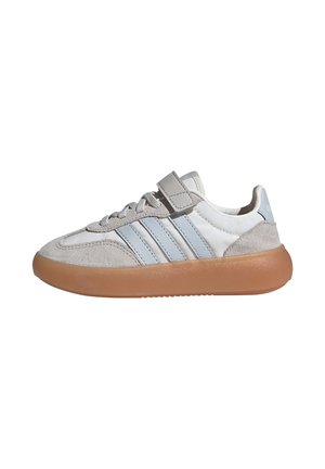 Sneaker blanche et grise avec trois rayures bleu clair, des accents en daim gris, une sangle Velcro et une épaisse semelle en caoutchouc marron.
