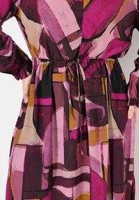 Chiffonkleid mit einem mehrfarbigen abstrakten Design in Rosa-, Violett- und Brauntönen. Verstellbarer Bindegürtel in der Taille, lange Ärmel.