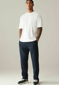 Camiseta blanca de manga corta combinada con pantalones tapered en color azul marino. El conjunto se complementa con zapatillas en blanco y negro. Tejido suave y ajuste relajado.