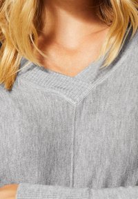 Grauer Strickpullover mit V-Ausschnitt, gerippter Textur und flachen Nähten, der einen weichen und leichten Stoff präsentiert.