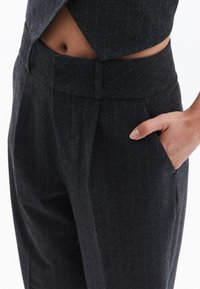 Pantaloni tailored grigio scuro con motivo a righe, vita alta e tasche laterali, caratterizzati da una texture liscia.