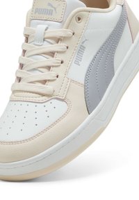 Puma-sneakers i vit, kräm och grått med perforerad tå, platta snöre, vadderad tunga och gummisula med texturerat mönster.