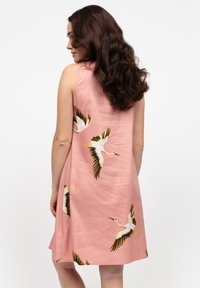 Abito senza maniche di colore rosa realizzato in tessuto leggero, con una fantasia di gru bianca, gialla e nera, caratterizzato da una forma A-line rilassata.