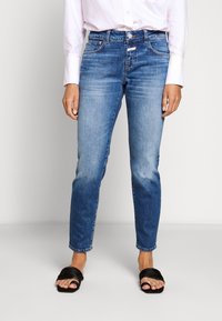 Ljust blå denimjeans med en figurnära passform, med hög midja, klassisk femfickdesign och diskret blekning. Matchade med svarta sandaler.