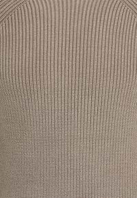 Tissu en maille beige clair, présentant un design textured à côtes avec des lignes verticales, offrant un léger éclat et un peu d'élasticité.