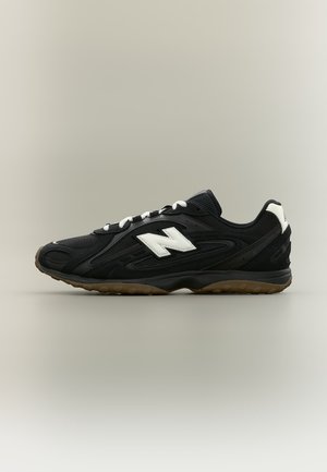 Chaussure de sport New Balance en noir et blanc avec dessus en mesh et synthétique, logo "N" blanc, et semelle en caoutchouc gomme, vue de profil.