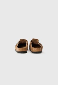 Smeđe suknje cipele na slip-on s teksturiranom površinom, s prilagodljivim trakama i crnom gumiranom potplatom.