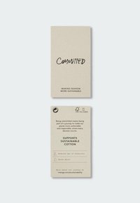 Étiquette engagée avec un texte promouvant le coton durable, la réduction des produits chimiques, l'économie d'eau et un lien vers un site web pour plus d'informations sur la durabilité.