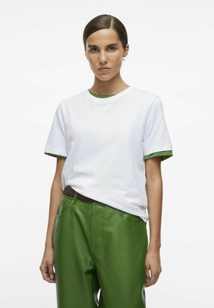 Witte T-shirt met groene kraag en mouwen, gecombineerd met groene leren broeken met een gestructureerde afwerking en zakken.