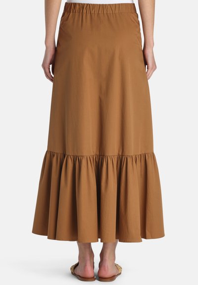Woman wearing a brown, ankle-length skirt with gathered ruffle hem and elastic waistband, shown from the back.