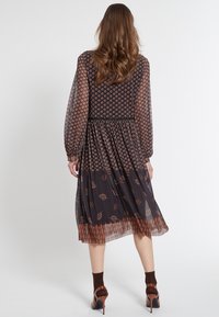 Lång, genomskinlig svart klänning med bruna mönster, elastisk midja och puffärmar. Lagerad nederdel med ett kontrasterande blommönster.