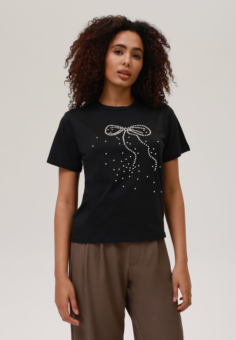 Sort t-shirt med korte ærmer, der har et bånddesign prydet med perler og spredte perler. Glat stof, afslappet pasform.