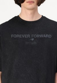 Black short-sleeve t-shirt made of soft fabric, featuring a crew neckline. The front has a contrasting print: "FOREVER FORWARD EST 1963."