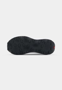 Semelle en caoutchouc noire avec surface texturée, présentant de grands crampons hexagonaux pour l'adhérence, et un détail d'accent rouge au talon.