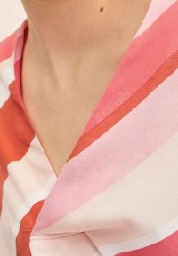 Blusa a righe rosa e corallo con scollo a V. Realizzata in un tessuto leggero e morbido; presenta un colletto pieghettato e una vestibilità comoda.
