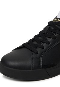 Čierna kožená teniska s zaoblenou špičkou, plochými čiernymi šnúrkami a čiernou gumovou podrážkou. Obsahuje zlaté logo na boku a ozdobné prešívanie.