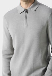 Lys grå, glidelås polo-genser laget av mykt stoff. Har en klassisk krage og glatt tekstur, designet for komfort.