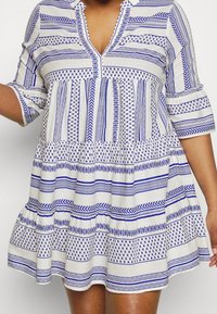 Vit klänning med blå geometriska och randiga mönster, med krage, knappslå och korta ärmar. Lättviktsmaterial, gathered kjol.