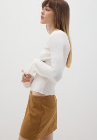 Top blanco de manga larga texturizado combinado con una minifalda de ante marrón. La parte superior tiene un cuerpo ajustado y mangas acampanadas.