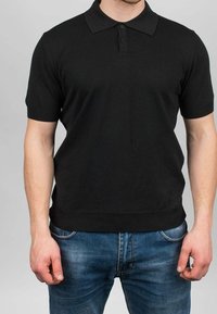 Polo nera a maniche corte realizzata in morbido cotone con una texture a coste, dotata di colletto classico e patta con tre bottoni.