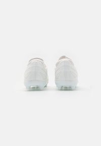 Scarpe da calcio bianche con una tomaia testurizzata, suola trasparente e ritagli geometrici sui lati. Presentano un design a profilo basso per garantire agilità.
