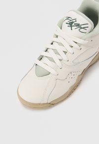 Jasno beżowe sneakersy z siateczkowymi wstawkami, białymi sznurówkami i zielonym akcentem na wyściełanym języku z wyszytym napisem "Flight". Teksturowana gumowa podeszwa.