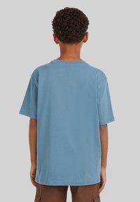 Camiseta de algodón azul cielo con mangas cortas, cuello redondo y un ajuste relajado. Presenta costuras mínimas y sin marcas visibles.