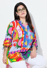 Blouse colorée et surdimensionnée avec des motifs mélangés comprenant des cœurs et des fleurs. Fabriquée en tissu léger avec un col en V et des manches froncées.