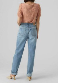 Pfirsichfarbener, strukturiert kurzärmeliger Oberteil kombiniert mit hellblauen, hoch taillierten Jeans, die umgeschlagene Säume und eine glatte Oberfläche haben. Beigefarbene Absätze runden das Outfit ab.