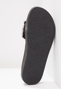 Sandale noire avec une semelle en caoutchouc texturée, au design simple et aux accents métalliques. Les vues latérales montrent des bords lisses et des contours confortables.