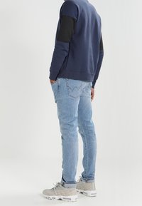 Světle modré džíny s úzkým střihem, se klasickým designem pěti kapes, spárované s námořnickou mikinou s tmavě šedými rukávy.