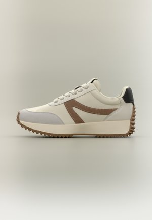 Bílo-šedé tenisky s hnědým akcentem, strukturované materiály, silná podrážka a zubatý vzor na spodní straně podrážky.